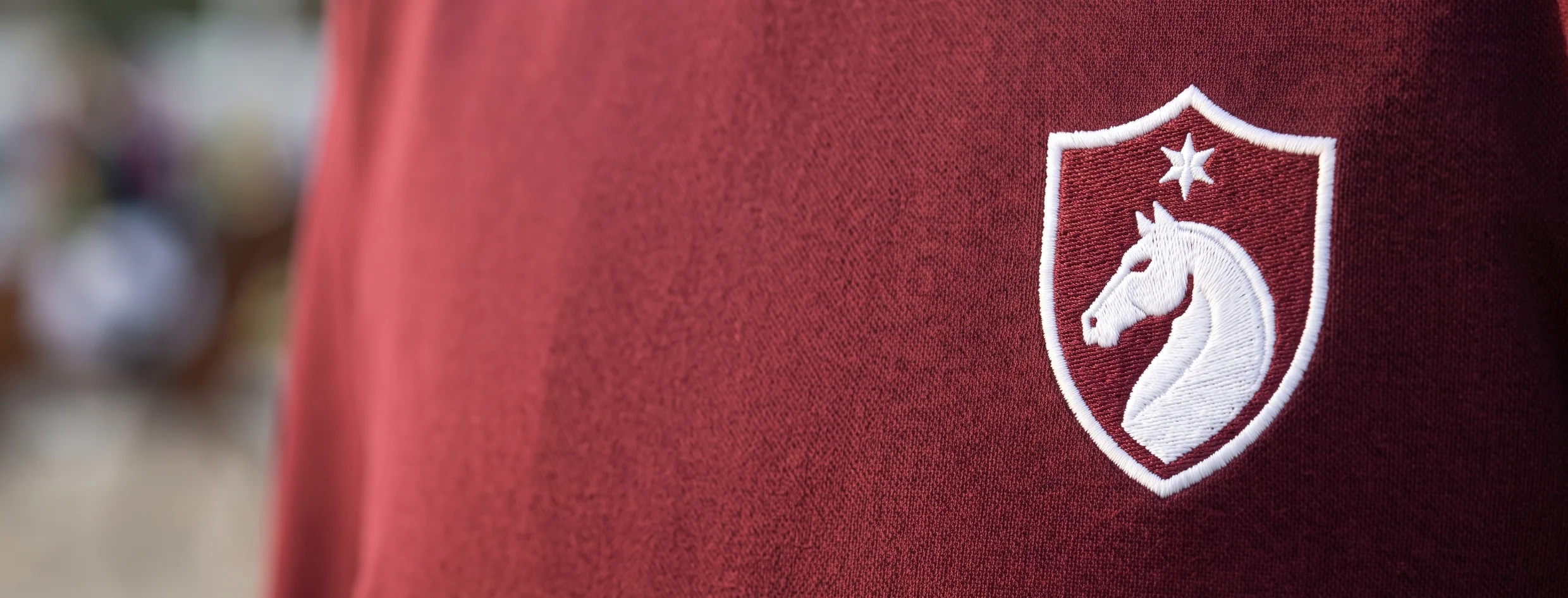 Escudo bordado del club en el pecho de una chaqueta de concurso granate